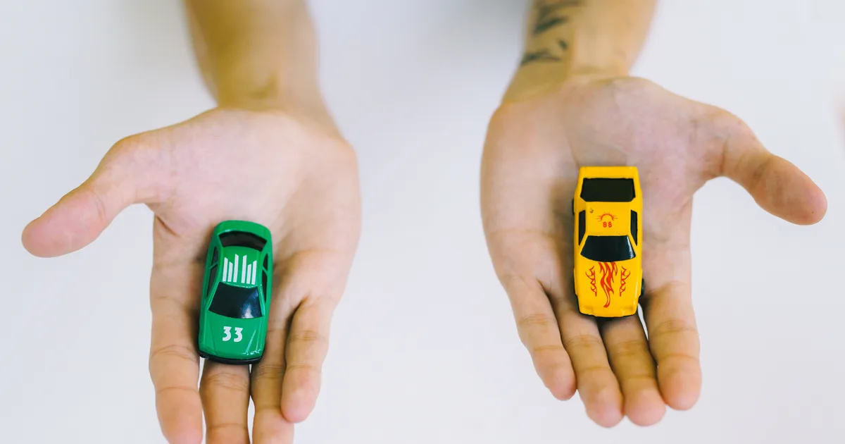 Deux mains ouvertes présentant chacune une voiture miniature, l'une verte, l'autre jaune, sur fond blanc