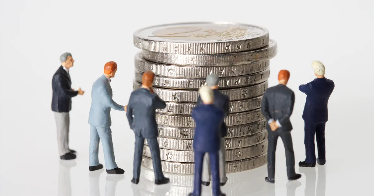 Figurines d'hommes d'affaires en costume rassemblées autour d'une haute pile de pièces