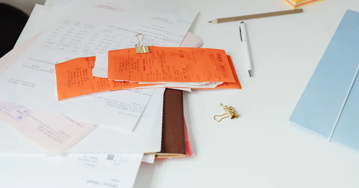 Tickets orange agrafés sur une pile de documents, à côté d'un stylo et d'une chemise bleue sur un bureau blanc
